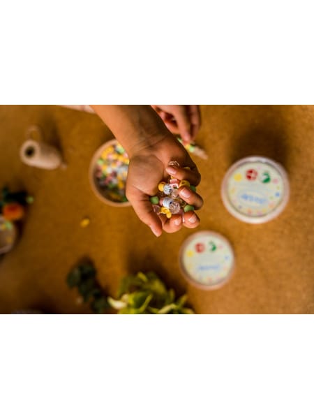 Personer sidder ved et bord og leger med små farverige perler, med gule blomster i baggrunden.